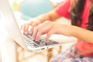 A young girl working with a lap top and her hands and fingers on keyboard .Light, bright interior.